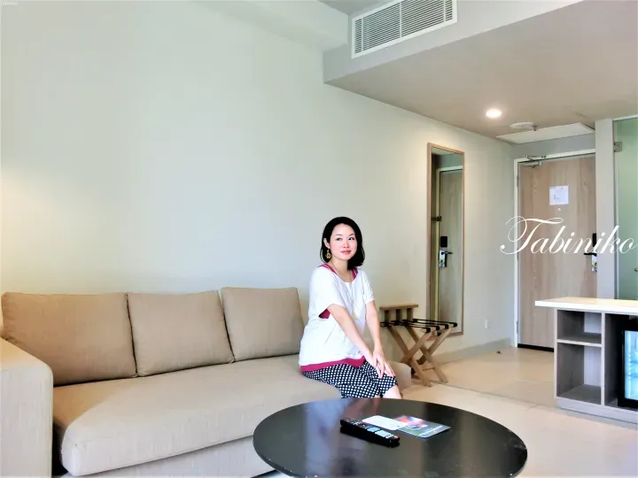 一名女子坐在現代酒店套房客廳的米色沙發上，前方有黑色咖啡桌和行李架。