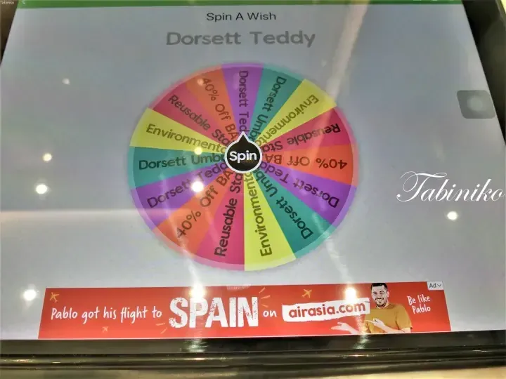 Dorsett Teddly promotional wheel with prizes like 40% off and reusable items, plus an AirAsia ad for flights to Spain.
