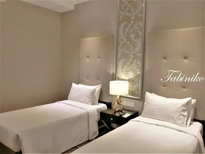 Twin beds with white linens and tufted headboards in a modern hotel room at Tabiniko