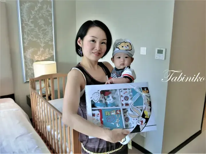 Woman holding a baby in a hotel room, displaying a Warner Bros. Bugs Bunny baby gift set.