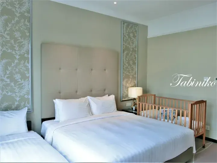 Hotel room with a large bed, white linens, and a wooden crib for families.