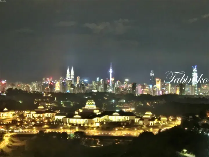 Night view of Kuala Lumpur skyline featuring Petronas Twin Towers and KL Tower, with National Mosque illuminated in foreground.