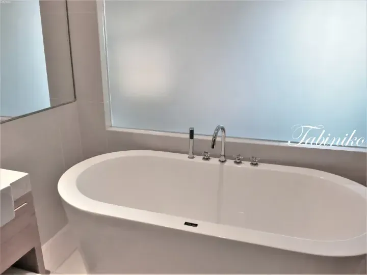 Modern white freestanding bathtub with chrome fixtures in a contemporary bathroom with frosted glass window