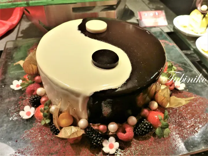 一款圆形蛋糕,饰有黑白阴阳图案,周围环绕着新鲜浆果和食用花卉。