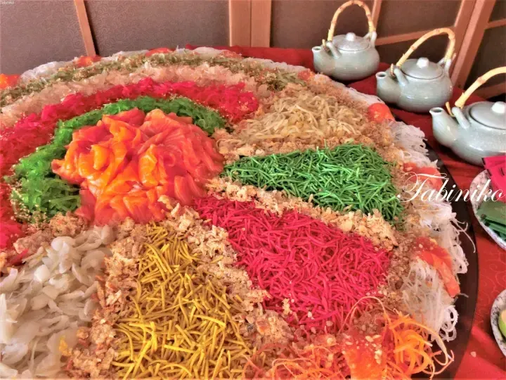 Colorful yusheng platter with salmon, shredded vegetables, and crispy toppings served with teapots.