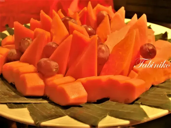 A decorative fruit platter featuring carved papaya slices and grapes arranged on a banana leaf.