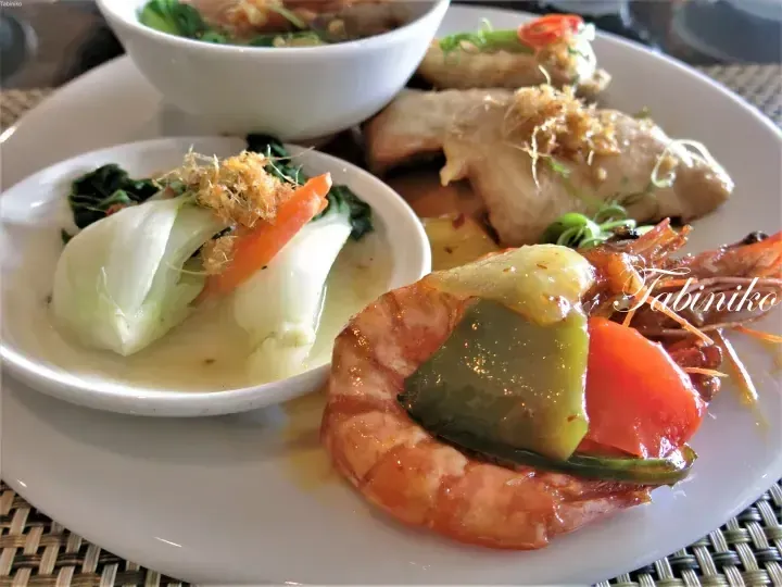 A plate of grilled prawns with vegetables and a side of steamed greens topped with fried shallots.