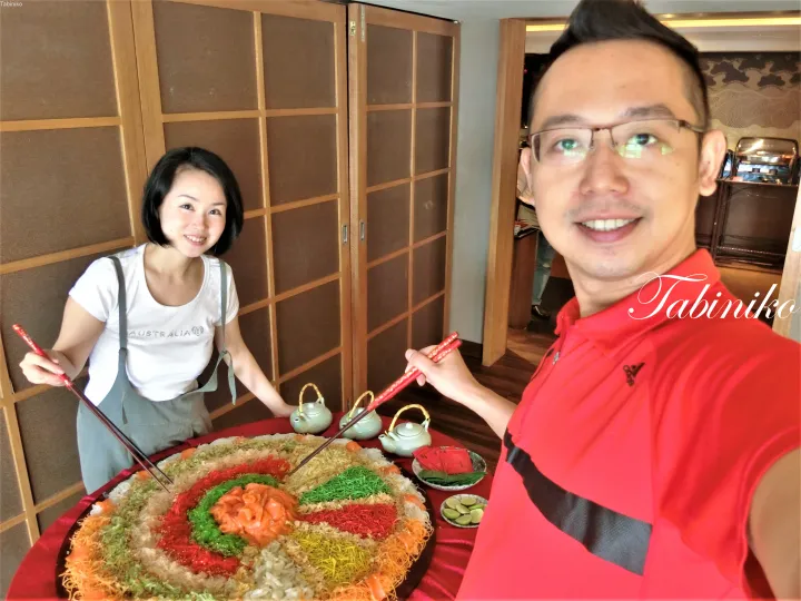 大きな彩り豊かなユッシェン（生魚のサラダ）の前で箸を持つカップル。