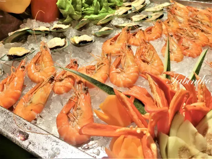 Fresh cooked prawns and mussels displayed on ice at a seafood buffet with decorative vegetable garnishes.