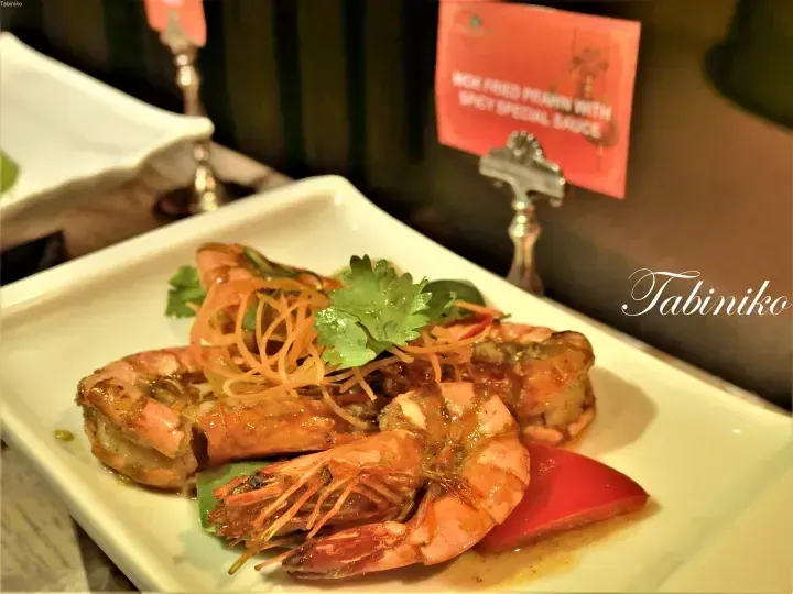 Wok fried prawn with spicy special sauce garnished with shredded carrots and cilantro on a white plate