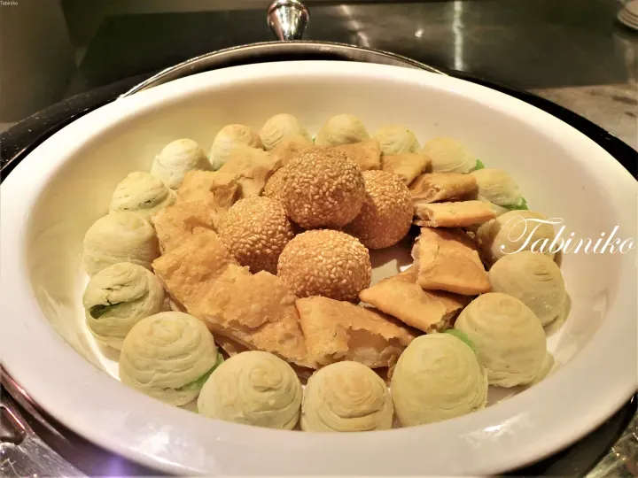 盛有芝麻球、酥皮点心和绿茶卷等各式糕点的白色碗。
