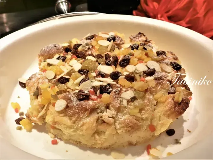 A slice of fruit cake topped with almonds, raisins, and candied fruits on a white plate.