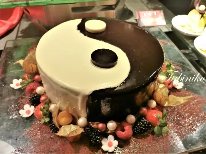 A round cake decorated with a black and white yin-yang design, surrounded by fresh berries and edible flowers.