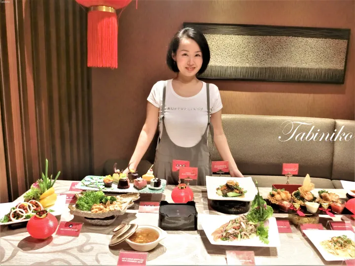 中華料理店のテーブルに並ぶ豪華な中国新年のビュッフェ料理の前で微笑む女性。