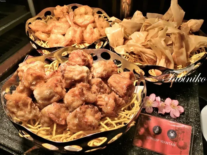 Fried shrimp wantan and dumplings served on noodles at a buffet, with a label reading Shrimp Wantan.