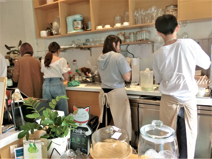 Staff preparing drinks behind a counter with a lucky cat sign and a chalkboard menu displaying Chinese characters.