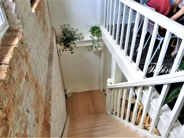 White staircase with wooden steps leading down to a lower level, featuring rustic stone walls and potted plants on a landing.