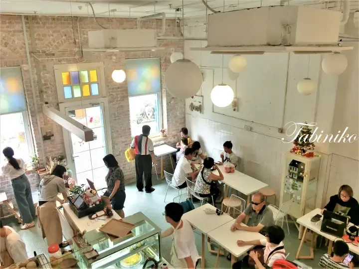 高角度拍摄的明亮咖啡馆内部，展示了裸露的砖墙、白色桌椅以及正在用餐的顾客。
