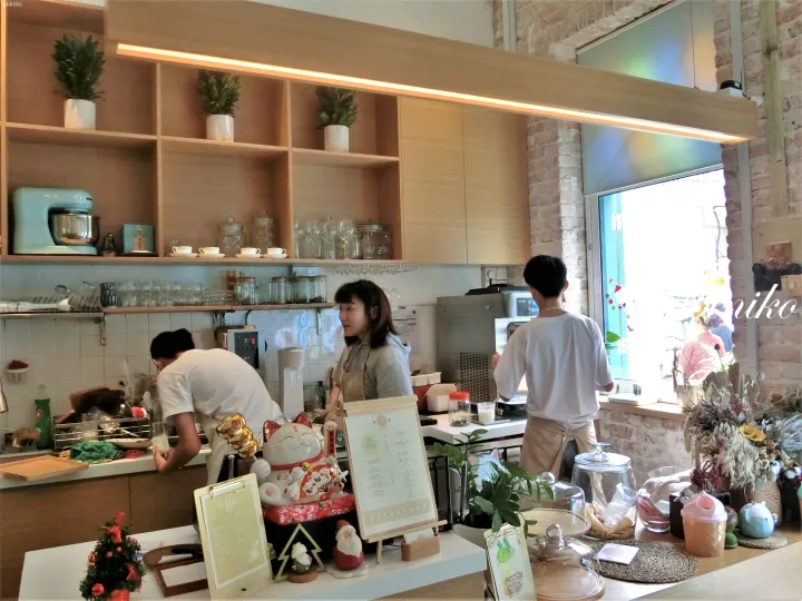 Baristas working behind the counter at a cozy cafe with wooden shelves, a lucky cat, and a menu stand.