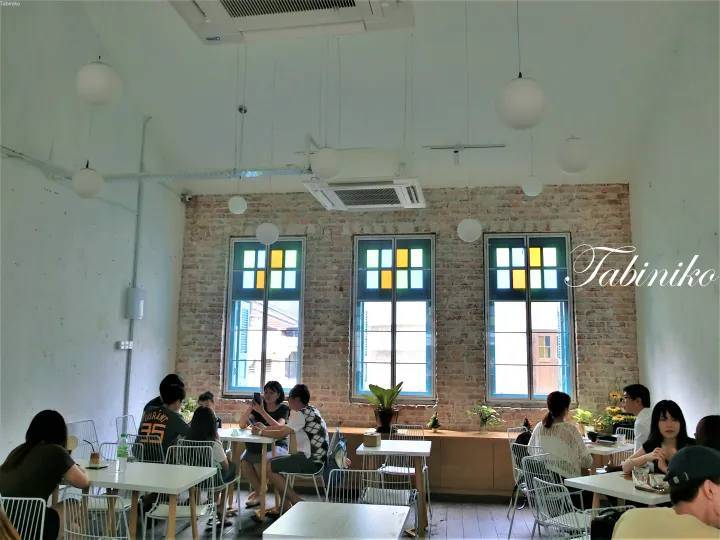 Interior of a cafe with exposed brick walls and colorful stained glass windows, where patrons are seated at white tables.