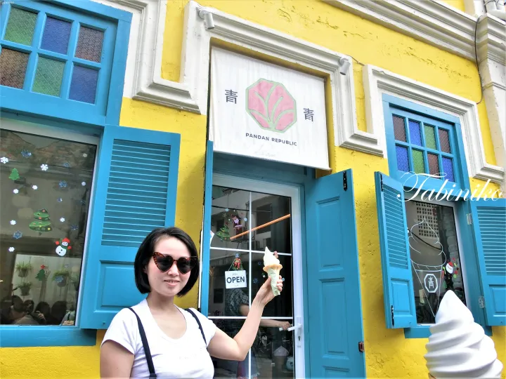 Woman holding pandan ice cream cone outside the yellow and blue Pandan Republic shop in Penang.
