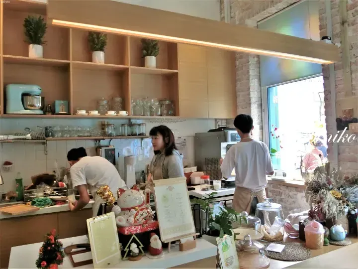 在一家装饰有木制架子和招财猫的舒适咖啡馆里，员工正在柜台后工作。