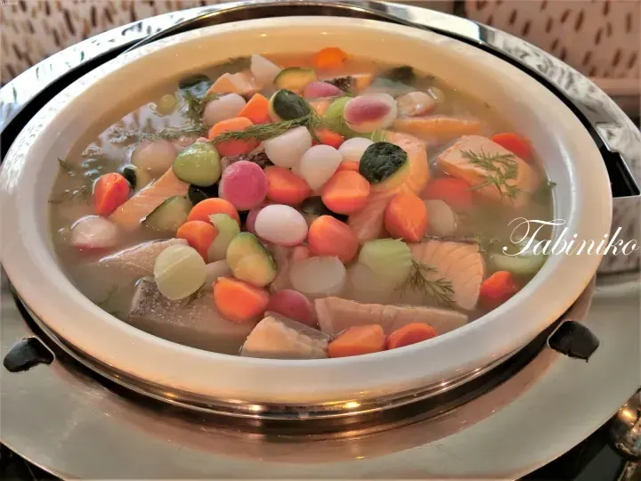 Salmon and vegetable soup served in a white ceramic bowl at a buffet station.