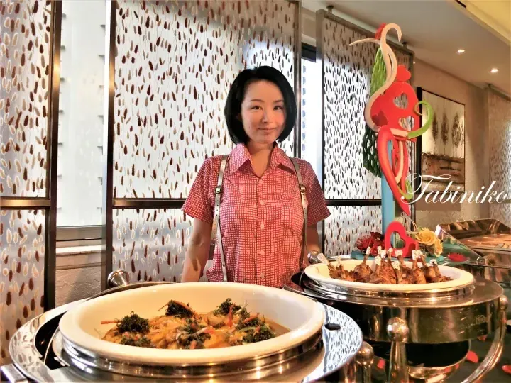 Woman in red checkered shirt standing behind buffet dishes at a dining area with patterned glass partitions.