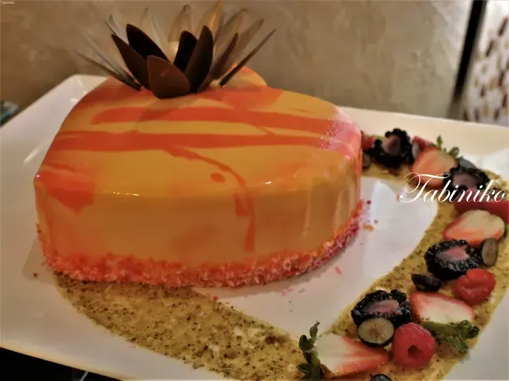 Orange glazed mousse cake with chocolate garnish and fresh berries on a white plate