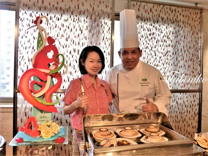 一位女士和行政總廚在擺放著土鍋料理和心形裝飾的自助餐台前豎起大拇指合影。