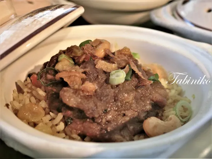 盛在白色陶瓷碗中的牛肉飯，上面撒有腰果和炸紅蔥頭。