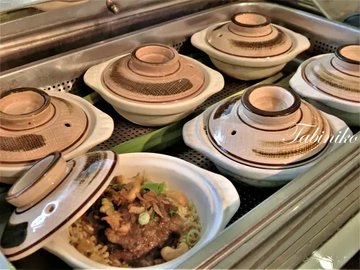 Assam rice served in traditional ceramic pots with lids, one open to reveal rice topped with meat and cashew nuts.