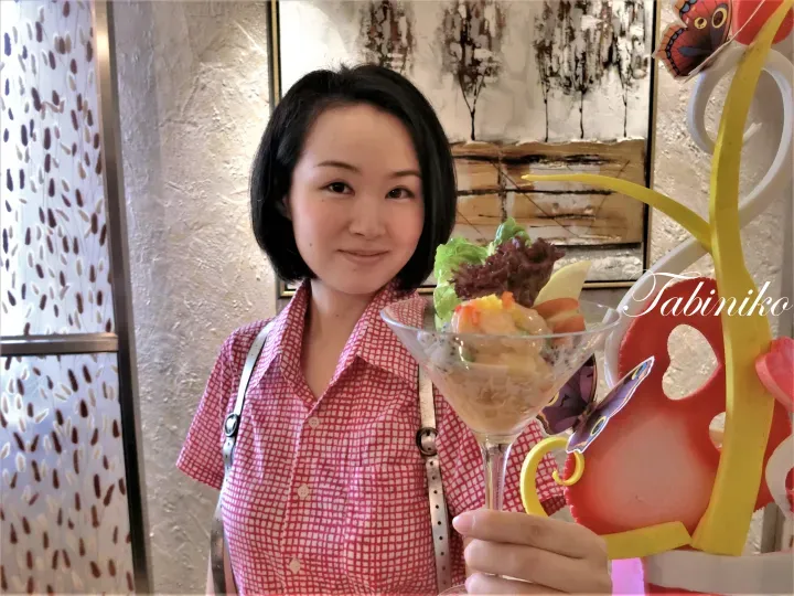 一名女子在咖啡廳手持盛有水果沙拉的馬天尼杯，旁邊有色彩鮮豔的蝴蝶裝飾。