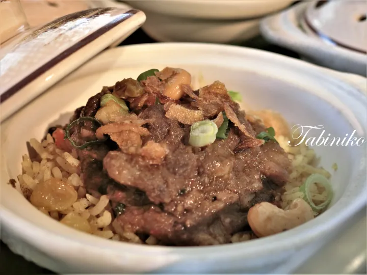 カシューナッツとエシャロットのフライをトッピングした、白い陶器のボウルに入った牛肉とご飯の料理。