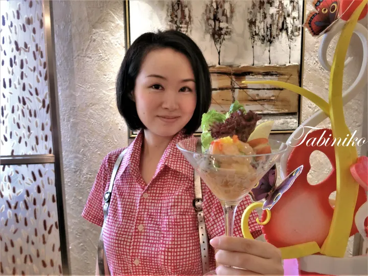 カフェでマティーニグラスに入ったフルーツサラダを持つ女性と、隣にあるカラフルな蝶の装飾。