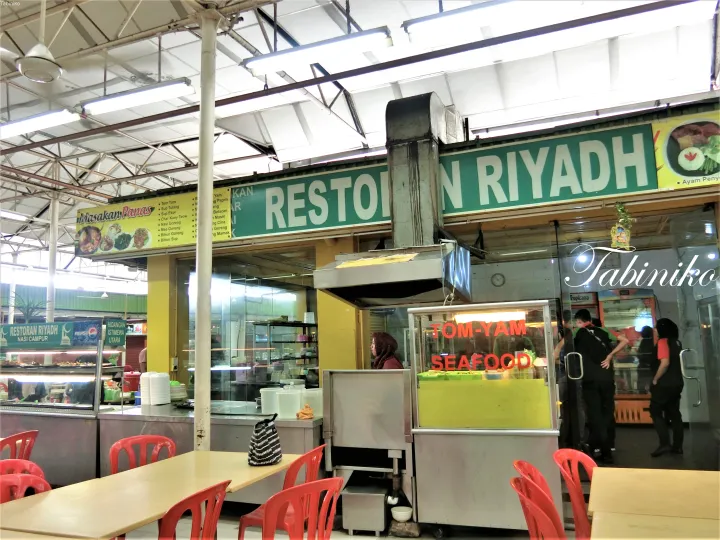 マレーシアのフードコートにあるRestoran Riyadhの店内。赤いプラスチック椅子とTom-Yam Seafoodの屋台が見えます。
