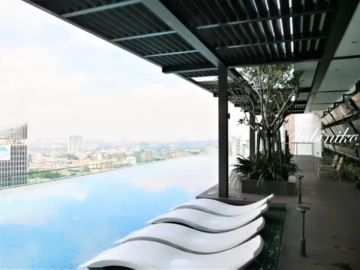 Infinity pool with lounge chairs overlooking Kuala Lumpur city skyline from a high-rise building.