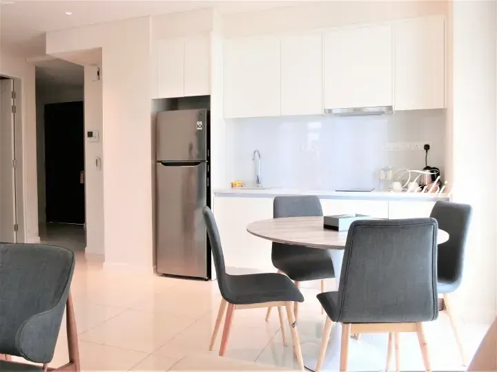 Modern kitchen with white cabinets, stainless steel refrigerator, and round dining table with grey chairs in a Malaysia apartment.