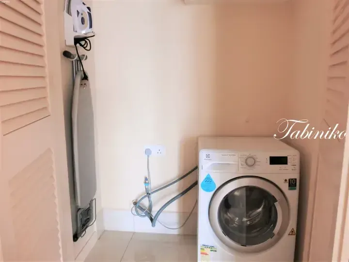 Electrolux washing machine in a laundry nook with a wall-mounted ironing board and louvered doors