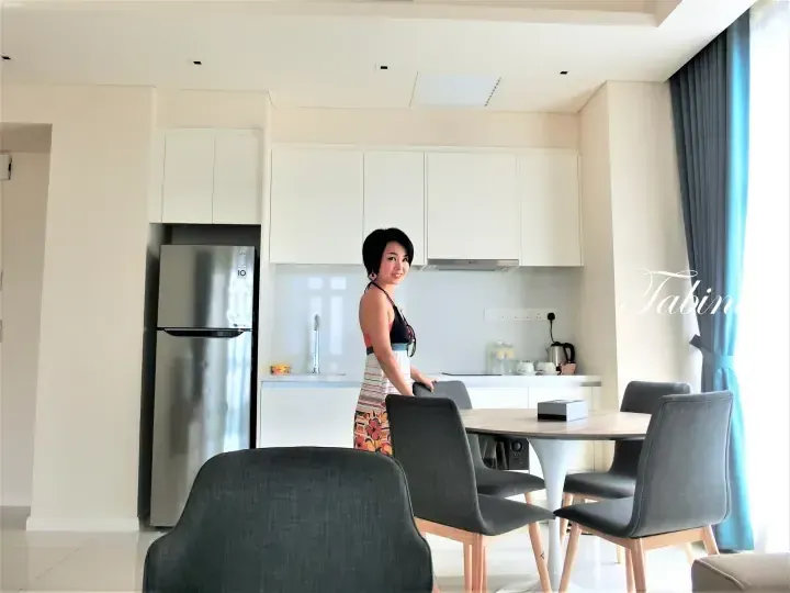 Woman in a colorful dress standing in a modern kitchen with white cabinets and a dining table.