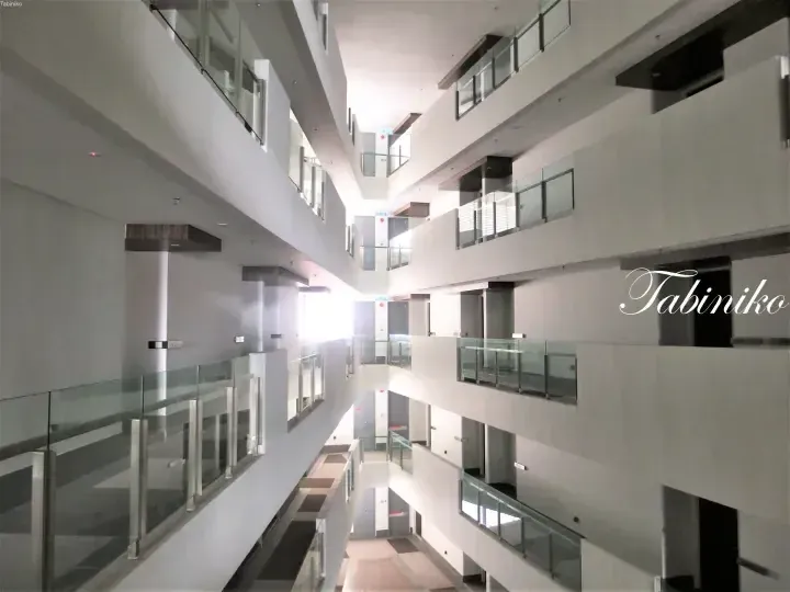 Modern multi-level atrium with glass railings and white walls, featuring the Tabiniko watermark.