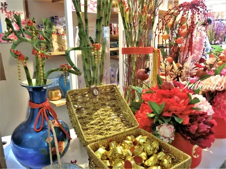 Decorative lucky bamboo and vibrant flowers arranged in vases alongside a golden basket filled with gold ingots for festive celebration.