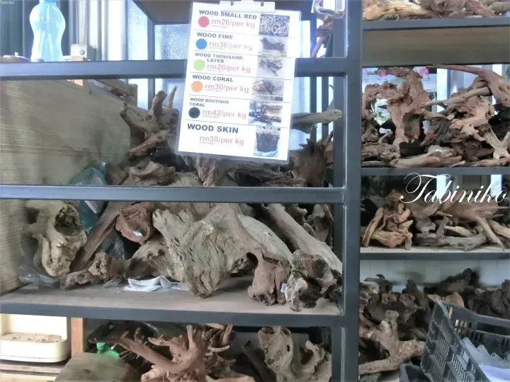 Shelves stocked with various types of driftwood for sale, with a price list showing options like Wood Small Red and Wood Fine.