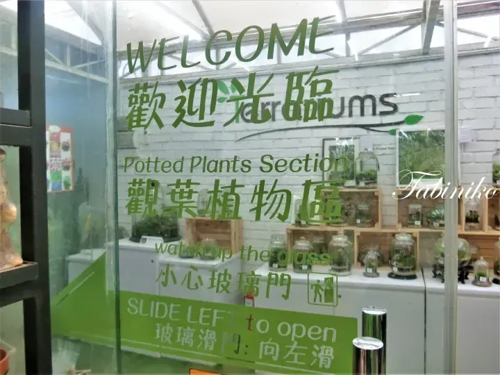 Glass door with green text welcoming visitors to the Potted Plants Section at Terrariums, featuring bilingual signage and a slide left instruction.