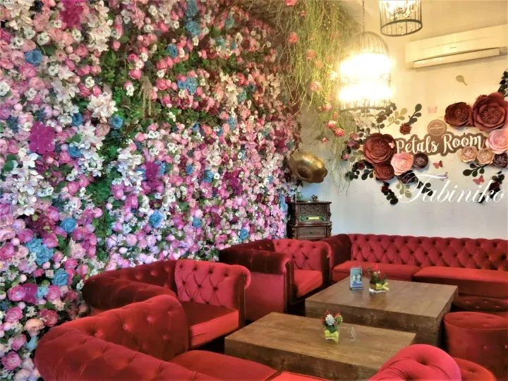 以鮮豔花卉牆為背景，擺放著紅色天鵝絨沙發和木桌的Petals Room舒適休息區。