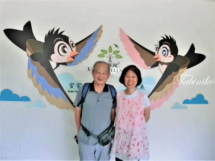 A couple poses in front of a wall mural featuring cartoon swallows and the Kuan Kung Swallow Park logo.
