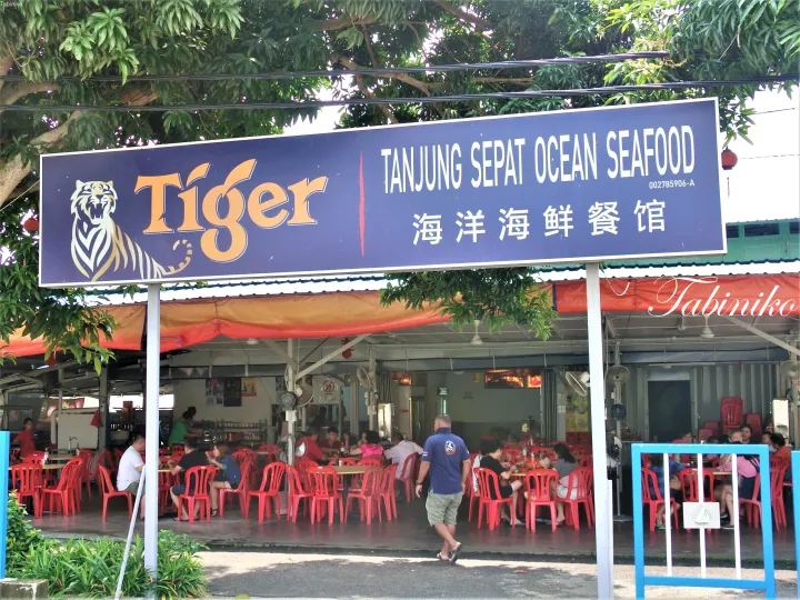 Tigerビールロゴが目立つTanjung Sepat Ocean Seafoodの看板と、赤い椅子が並ぶ屋外飲食店の様子。