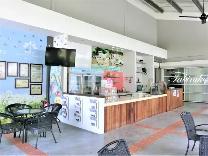 Kuan Wellness ecopark cafe interior with wooden counter, display fridge, and seating area.