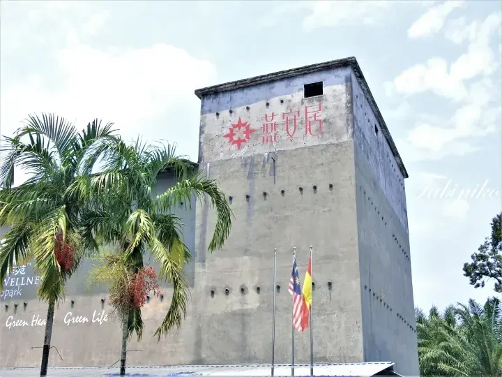 Concrete building facade with Yan An Ju logo, Malaysian flags, and palm trees at a wellness property.