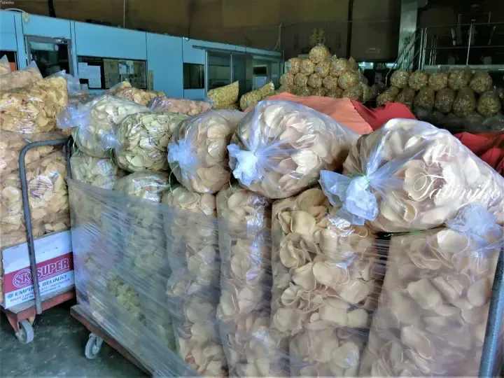 Large bags of crispy crackers stacked on a trolley in a warehouse, with boxes labeled SK Super Belinjo visible nearby.
